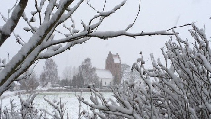Snødekte træer foran kirke i snefaldende landskab