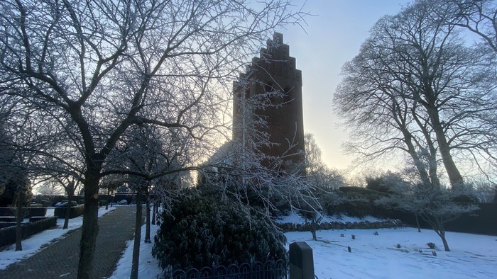 En snedækket park med en højtårnet kirke i baggrunden