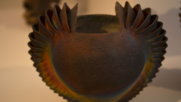 Indviklet keramikskål med en kamformet kant, der udviser iridescerende, flerfarvede refleksioner.