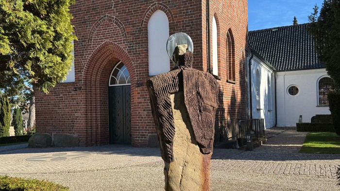 En slående stenskulptur af en klædt figur står foran indgangen til en murstenskirke.