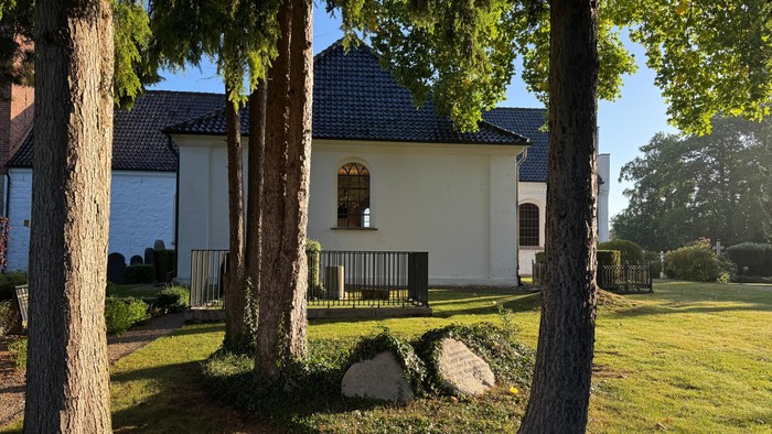 Hyggelig hvid kapel omgivet af høje træer i en fredelig, grøn eng.