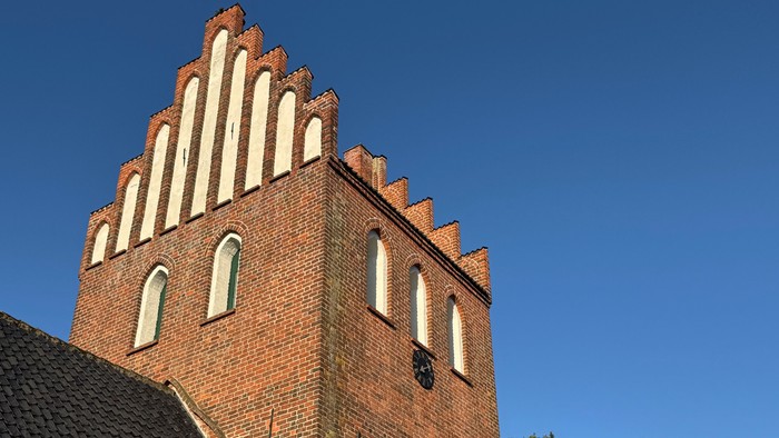 Historisk murstenskirketårn med karakteristisk trappegavl og buede vinduer under klar blå himmel.