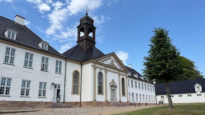 Elegant historisk bygning med et centralt klokketårn og symmetrisk hvid facade omgivet af grønne græsplæner.
