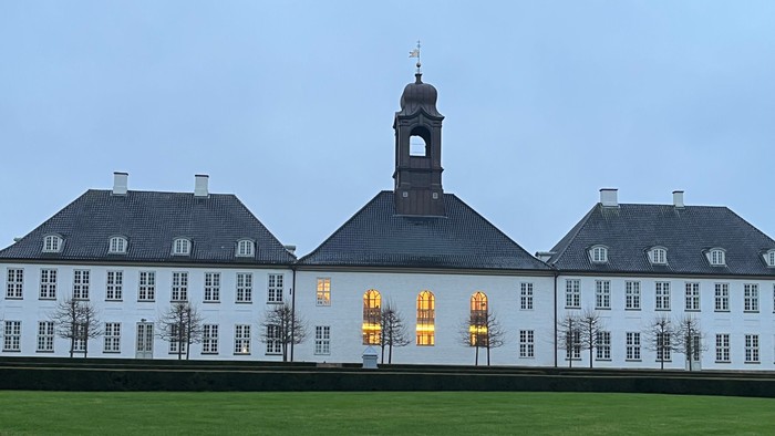 Elegant hvid herregård med centralt klokketårn, oplyste vinduer og velplejet grøn græsplæne.