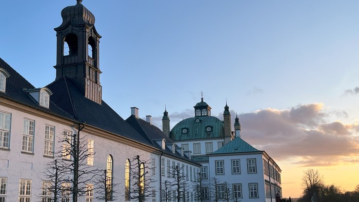 Stor historisk bygning med tårn og kuppelsaler ved solnedgang