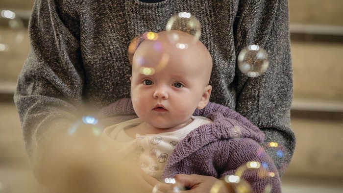 Et barn i en graur trøje holder et spæd barn, der ser opad.
