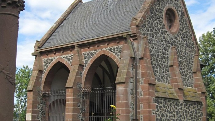 Ein kleines, verwittertes Ziegelgebäude mit spitzen Bögen und einem schrägen Dach.