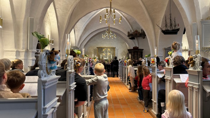 En gruppe mennesker, der deltager i en gudstjeneste i en prægtig, hvælvet kirke med kirkebænke og dekorative elementer.