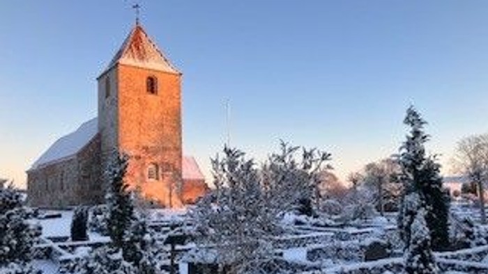 En kirke med tårn og klokke i snefuld landskab