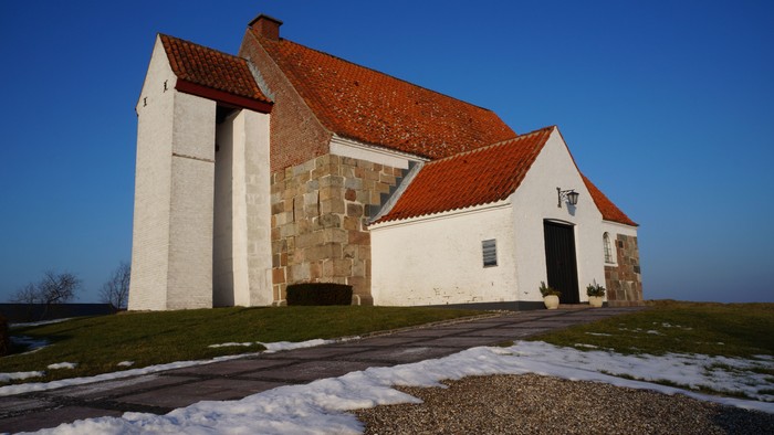 En lille, hvidkalket kirke med røde tag og en smal vej foran