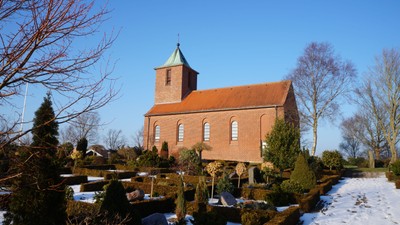 En rød murstenskirke med tårn i snødekt landskab