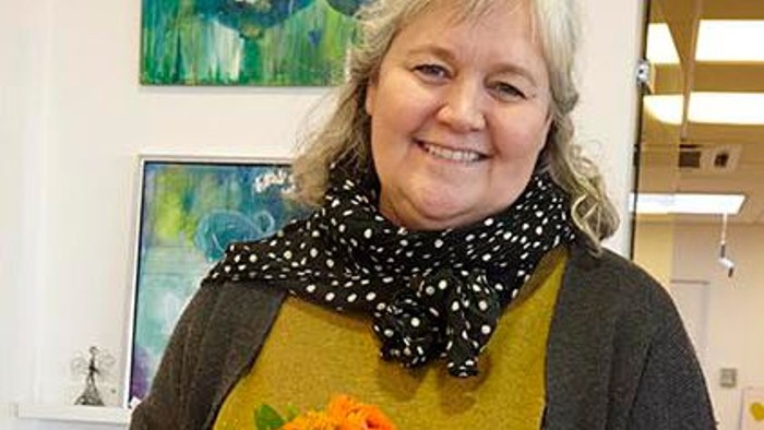 Kvinde holder en blomstertand og smiler.