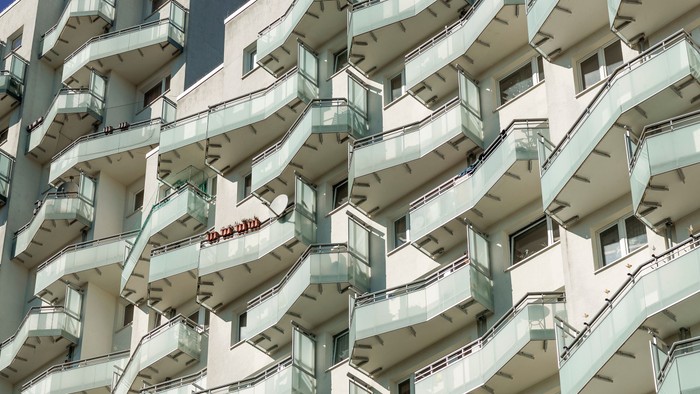 Modernes, geschwungenes Wohngebäude mit Glasgeländern und einem sichtbaren roten Schild auf einem Balkon.