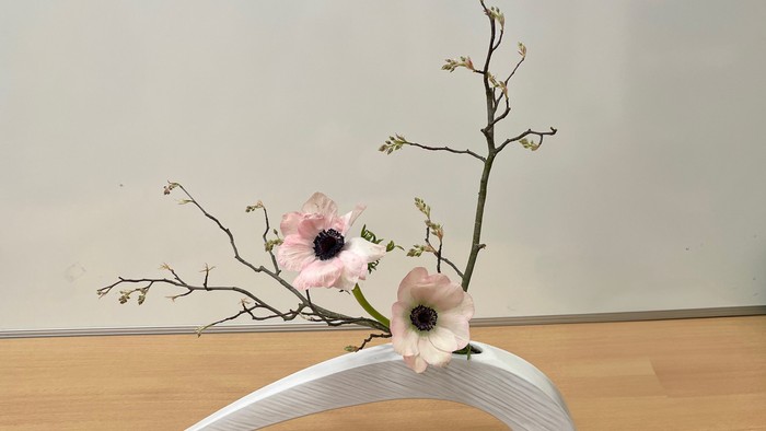 Ein weißer Blumenhalter mit zwei rosa Blumen auf einem Holzboden