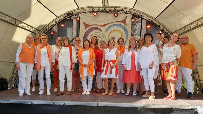 Gruppe von Menschen in orange-weißer Kleidung, die auf der Bühne posieren.