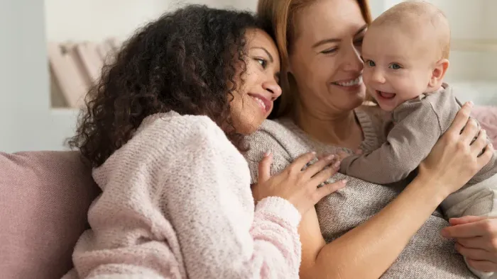 Zwei Frauen und ein Baby sitzen zusammen auf einem Sofa und lächeln.