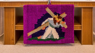 Ein Altar mit einer pinken Decke und einem Kreuz, umgeben von Kerzen und Blumen.