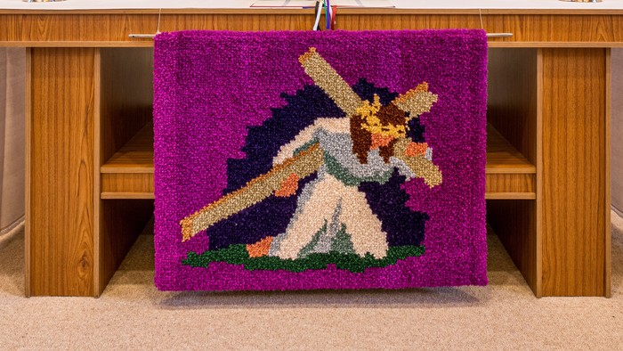 Ein Altar mit einer pinken Decke und einem Kreuz, umgeben von Kerzen und Blumen.