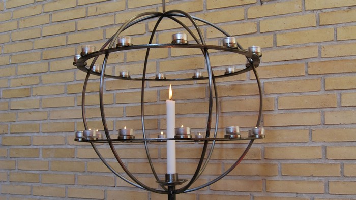 En globusformet kandleholder med flere lyse candler foran mur af røde mursten