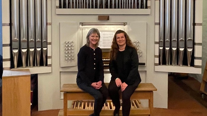 To personer poser sammen foran et stort pibeorgel i en kirke.