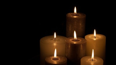 Fem tændte lys i forskellige højder mod en mørk baggrund.