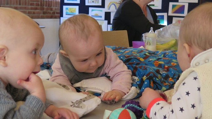 Tre små børn spiller med legetøj på en bænk.