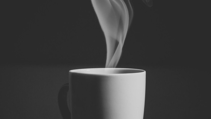 En hvid tekop i sort lys og skygge med røg.