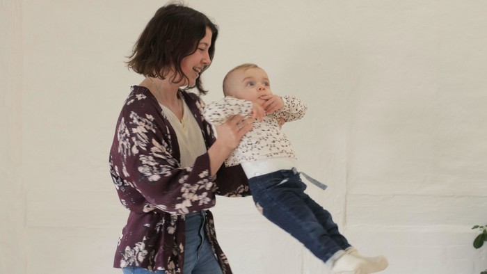 En kvinde holder et spæd barn i hendes arm, begge smiler.