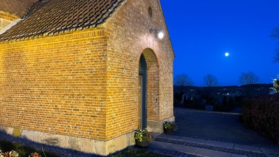 En lille murstenskirke belyset ved natten med en halvmåne i himlen