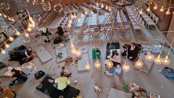 Stor hall med mange bord og belysninger, folk sidder og spiser.