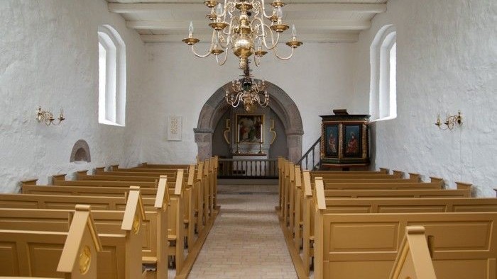 Indre del af kirke med guldfarne bænke og hængende lysekone