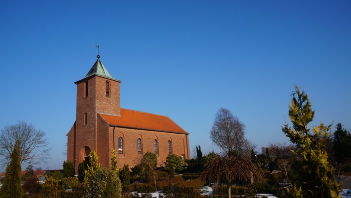 Røde kirke med tårn og spiret, omgivet af snedækkede træer og buske