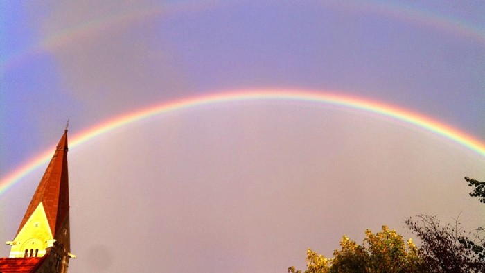 Regnbue over kirke med spiret.