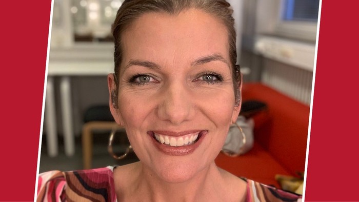 Kvinde med kort hår, der smiler, iført en mønstret top på en rød baggrund.