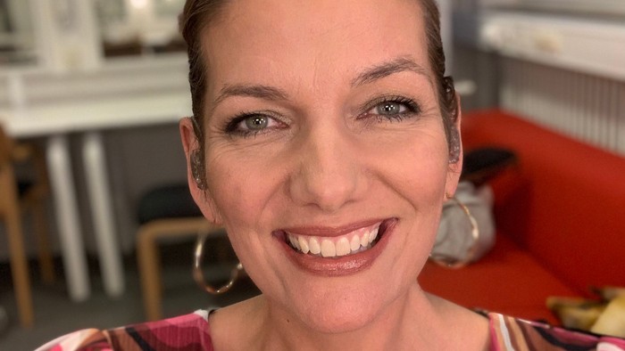 En kvinde smiler indendørs iført en farverig top.