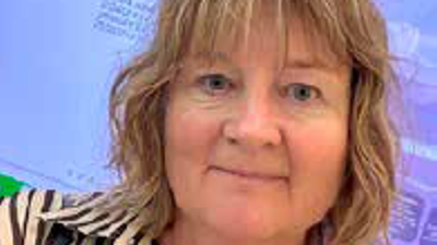 En kvinde med kort blondt hår, der smiler foran en blå baggrund.