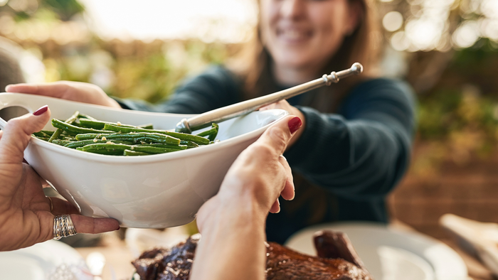 Folk, der serverer grønne bønner fra en skål under et måltid med stegt kalkun.