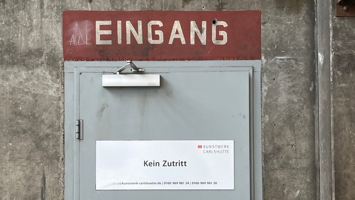 Graue Metalltür mit der Aufschrift „All Eingang“, „Kein Zutritt“ und den Kontaktdaten von Kunstwerk Carlshütte.