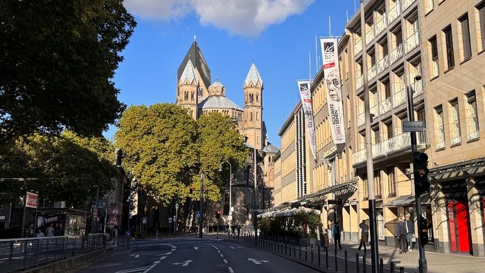 Straße in der Stadt gesäumt von einer historischen Kathedrale und modernen Gebäuden unter einem klaren blauen Himmel.