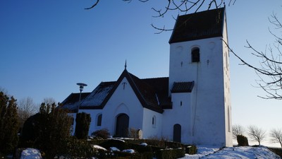 Hvid kirke med højt tårn i snelandskab.