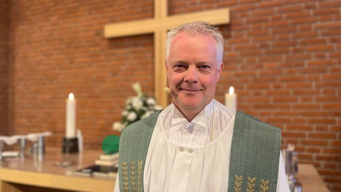 Mand i hvid liturgisk klæde foran alter med kors og lysstake