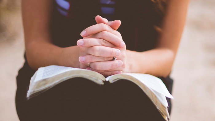 En person sidder på en strand med håndene samlet i skønt.