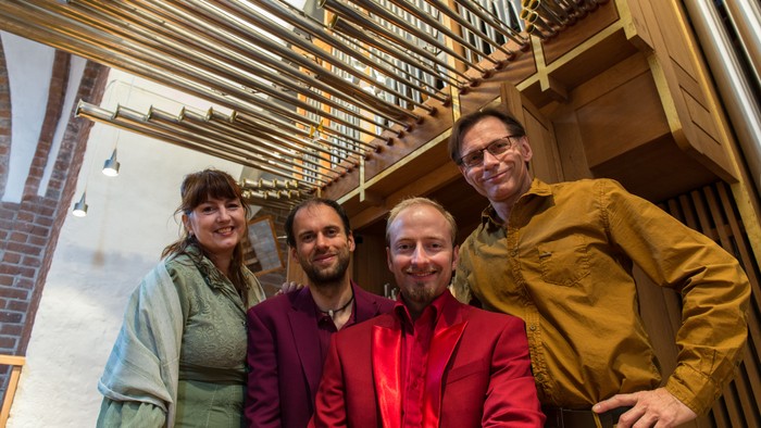 Fire personer poser sammen foran orgelpiber.