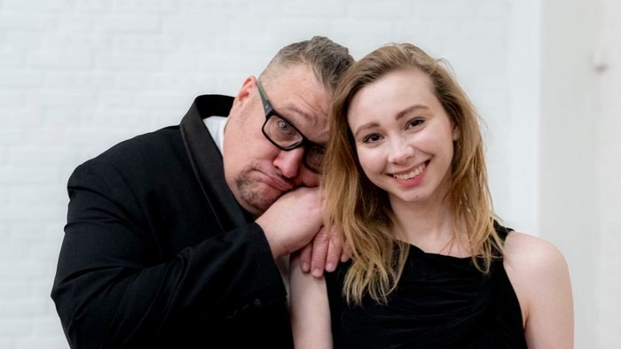 En mand med briller læner sig kærligt op ad en smilende kvinde i en sort kjole.