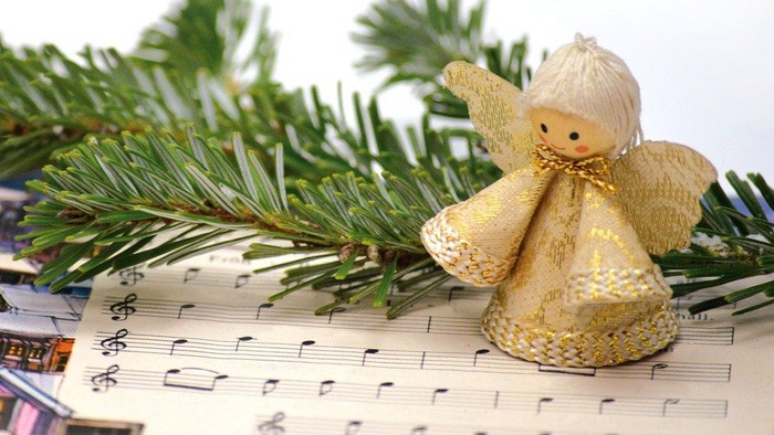Ein goldener Engel sitzt auf Notenblättern neben einem Tannenzweig