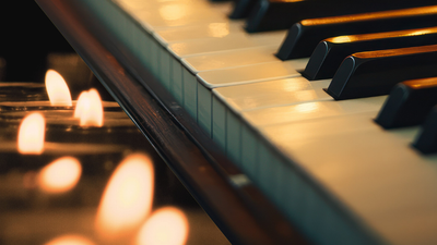 Nærbillede af oplyste klavertangenter med stearinlys, der kaster et varmt, flakkende lys nedenunder.