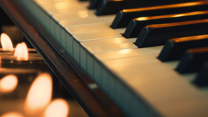 Nærbillede af oplyste klavertangenter med stearinlys, der kaster et varmt, flakkende lys nedenunder.