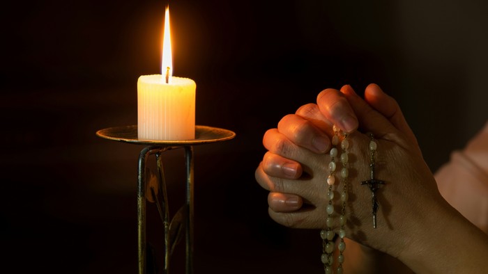 Ein friedvoller Moment mit betenden Händen, die Rosenkranzperlen halten, neben einer brennenden Kerze.