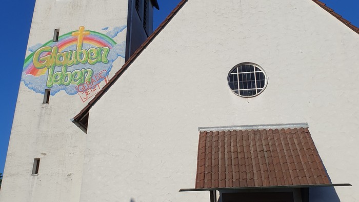 Weiße Kirche mit buntem Schild und Holztür.