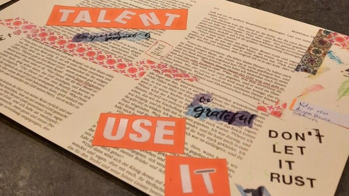 Kreativer Werkstatttisch mit Kunstmaterialien und motivierenden Zeitungsausschnitten mit der Aufschrift: *„Talent: Nutze es, lass es nicht rosten.“*